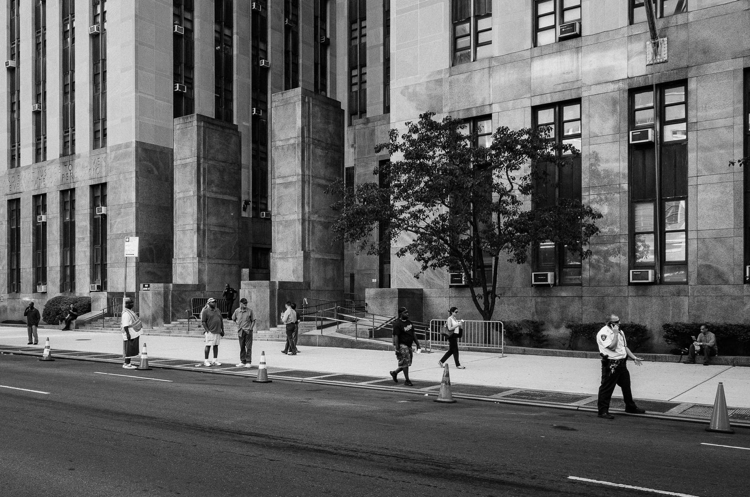 Art deco architectural details on a historic government building's facade with pedestrians walking past on the sidewalk.