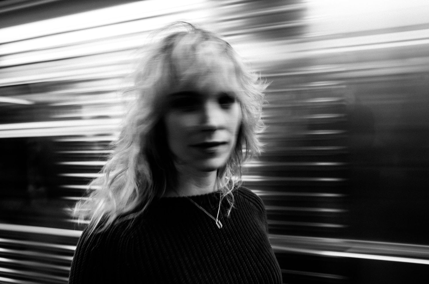 Black and white motion blur portrait with metallic striped background creating dynamic visual effect.