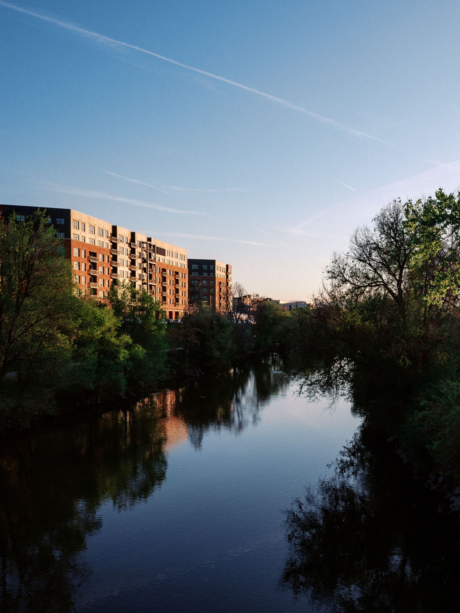 Waterfront apartment complex reflecting in calm lake waters during sunset.