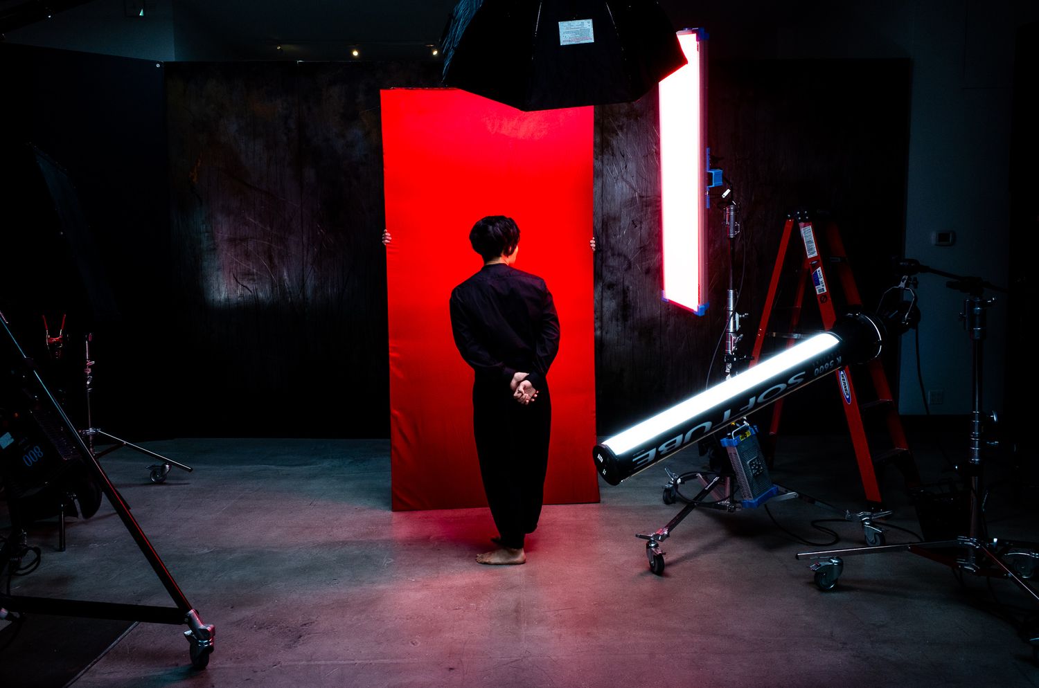 Silhouette figure standing in front of bright red doorway on dark studio set with lighting equipment.