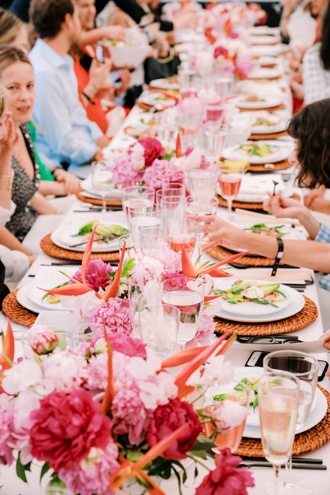Elegant outdoor dining table with pink peony floral centerpieces, wicker chargers, and rose champagne glasses.