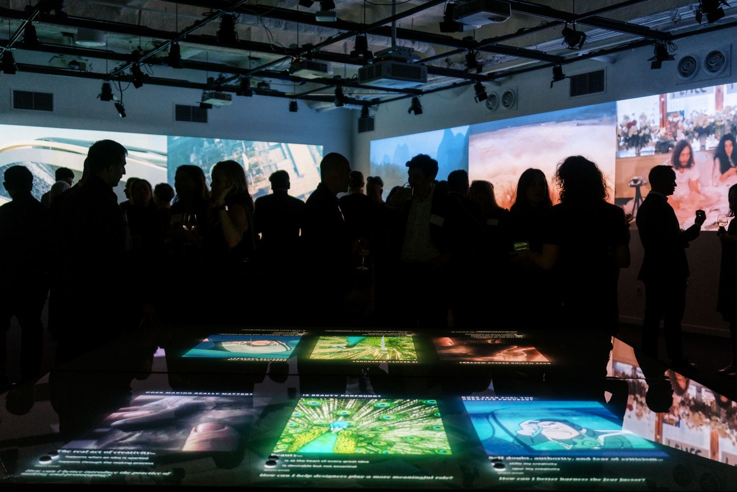 Silhouettes of visitors viewing illuminated floor displays at an immersive multimedia exhibition.