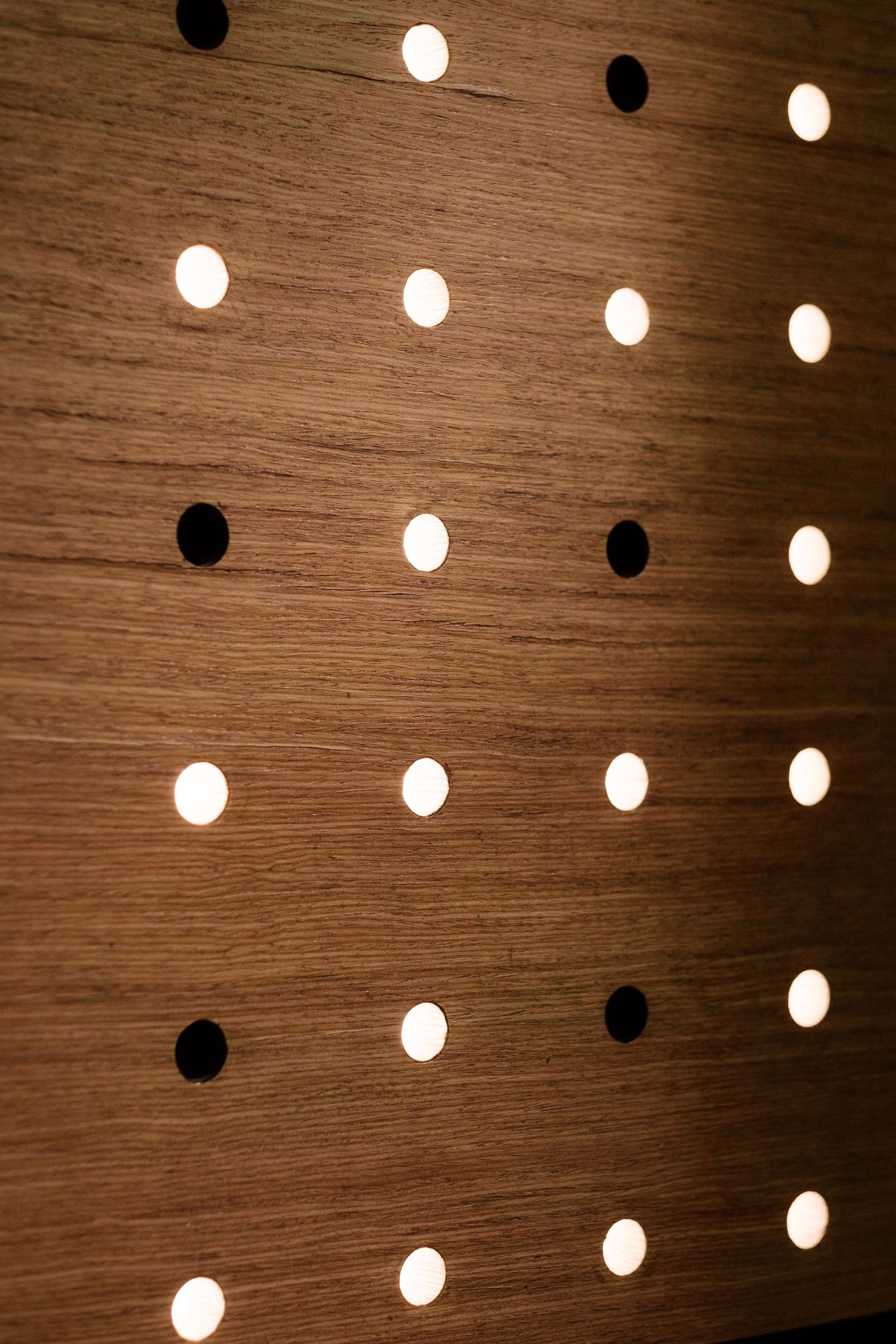 Wooden wall panel with artistic arrangement of circular light fixtures creating pattern.