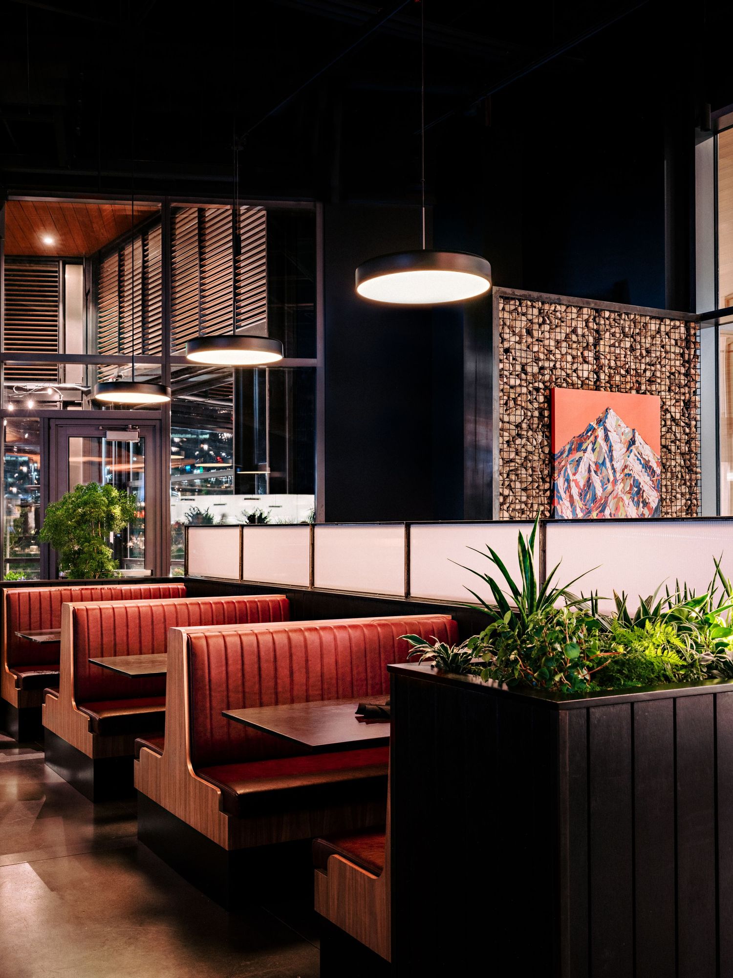 Modern restaurant interior with red leather booths, pendant lights, and decorative wall art.