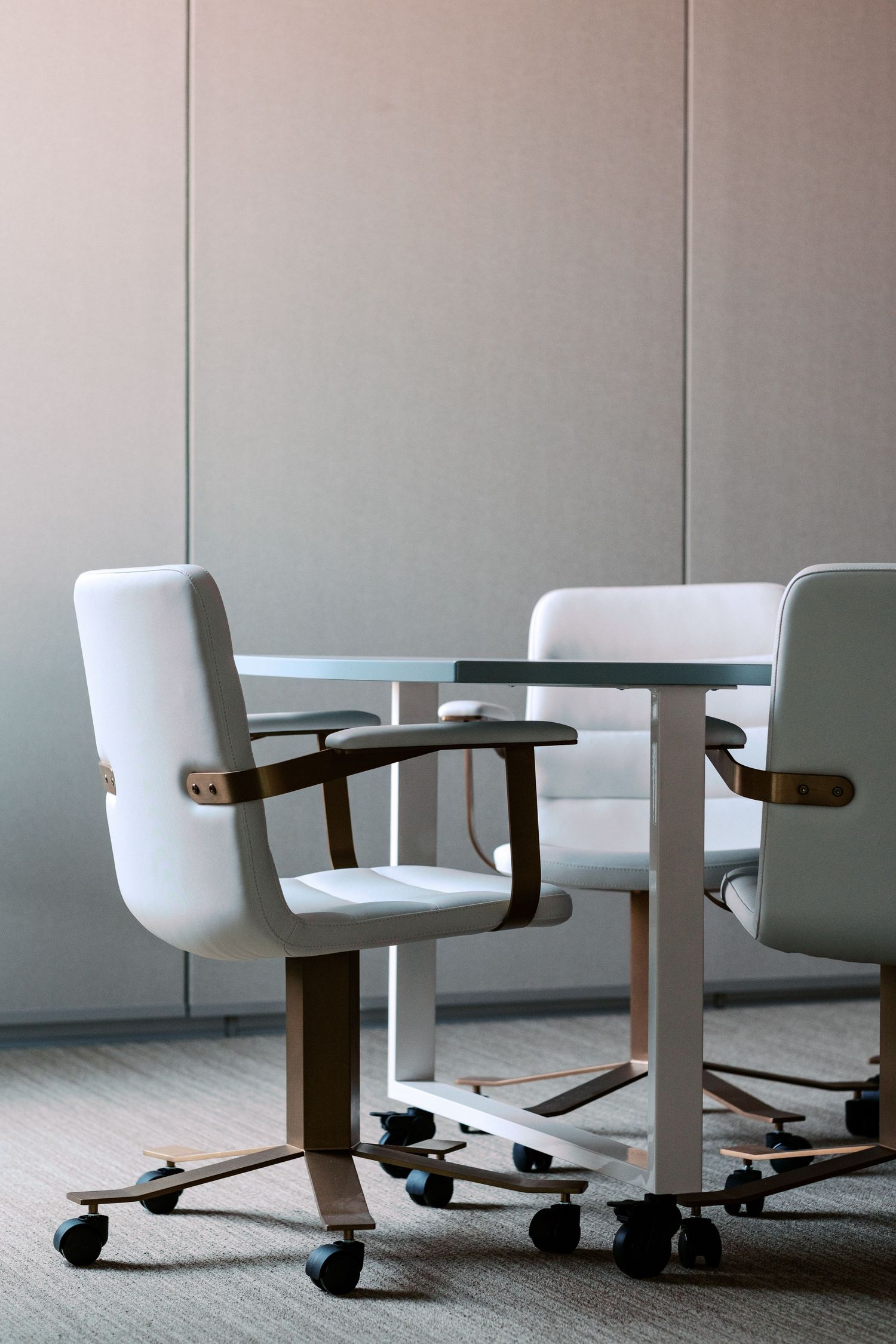 White office chairs with wooden armrests arranged around a conference table in a minimalist setting.