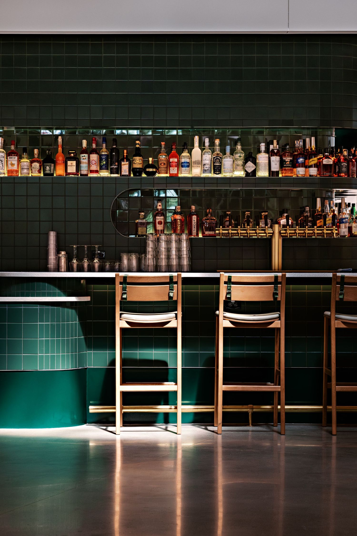 Modern bar interior with illuminated shelving and sleek bar stools in dark ambiance.