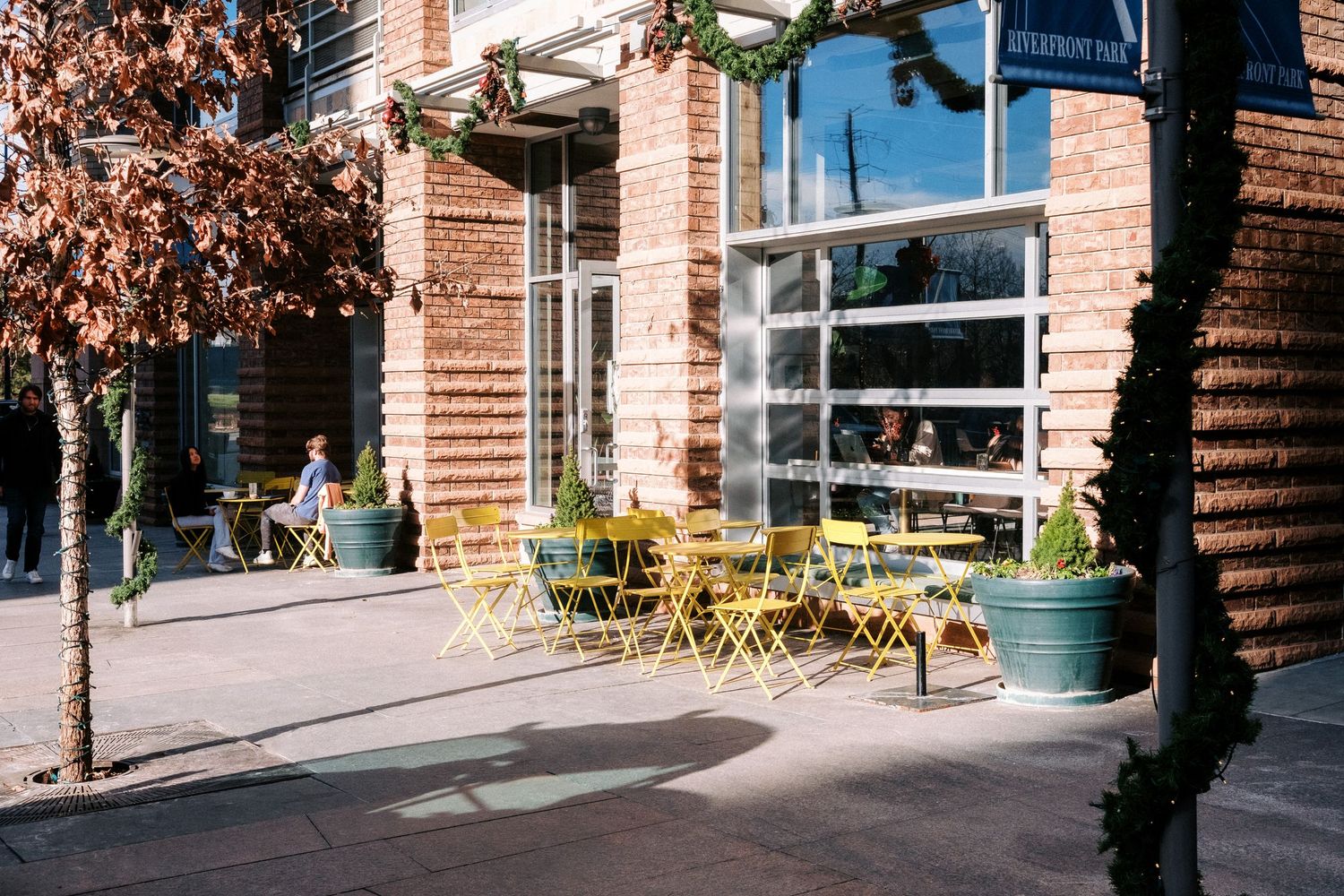 Yellow cafe chairs and tables line the sidewalk outside a brick building on a sunny day.