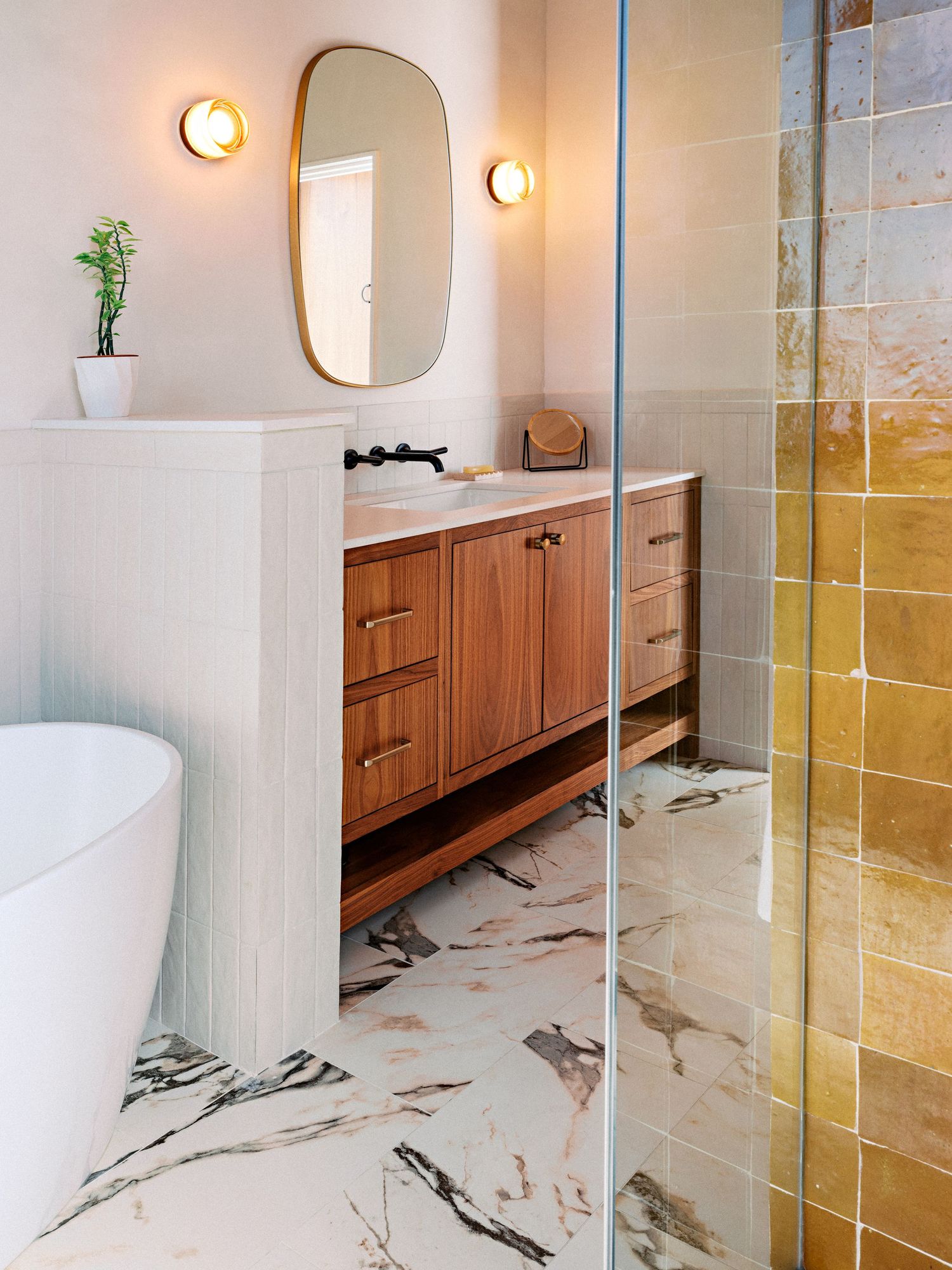 Luxurious bathroom featuring marble floors, wooden vanity, and freestanding tub with gold fixtures.