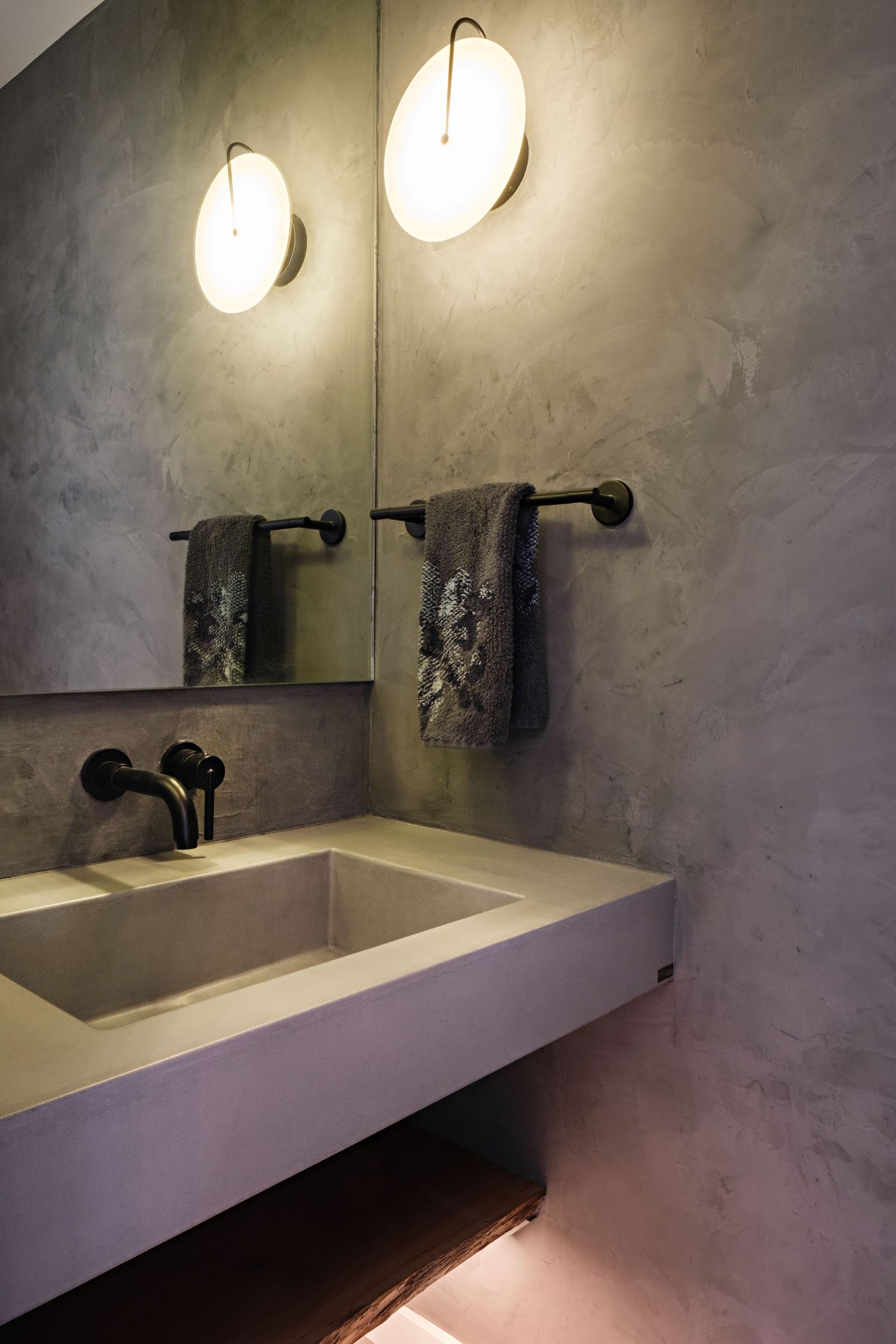 Minimalist bathroom vanity with concrete walls, floating sink, and round pendant lighting.