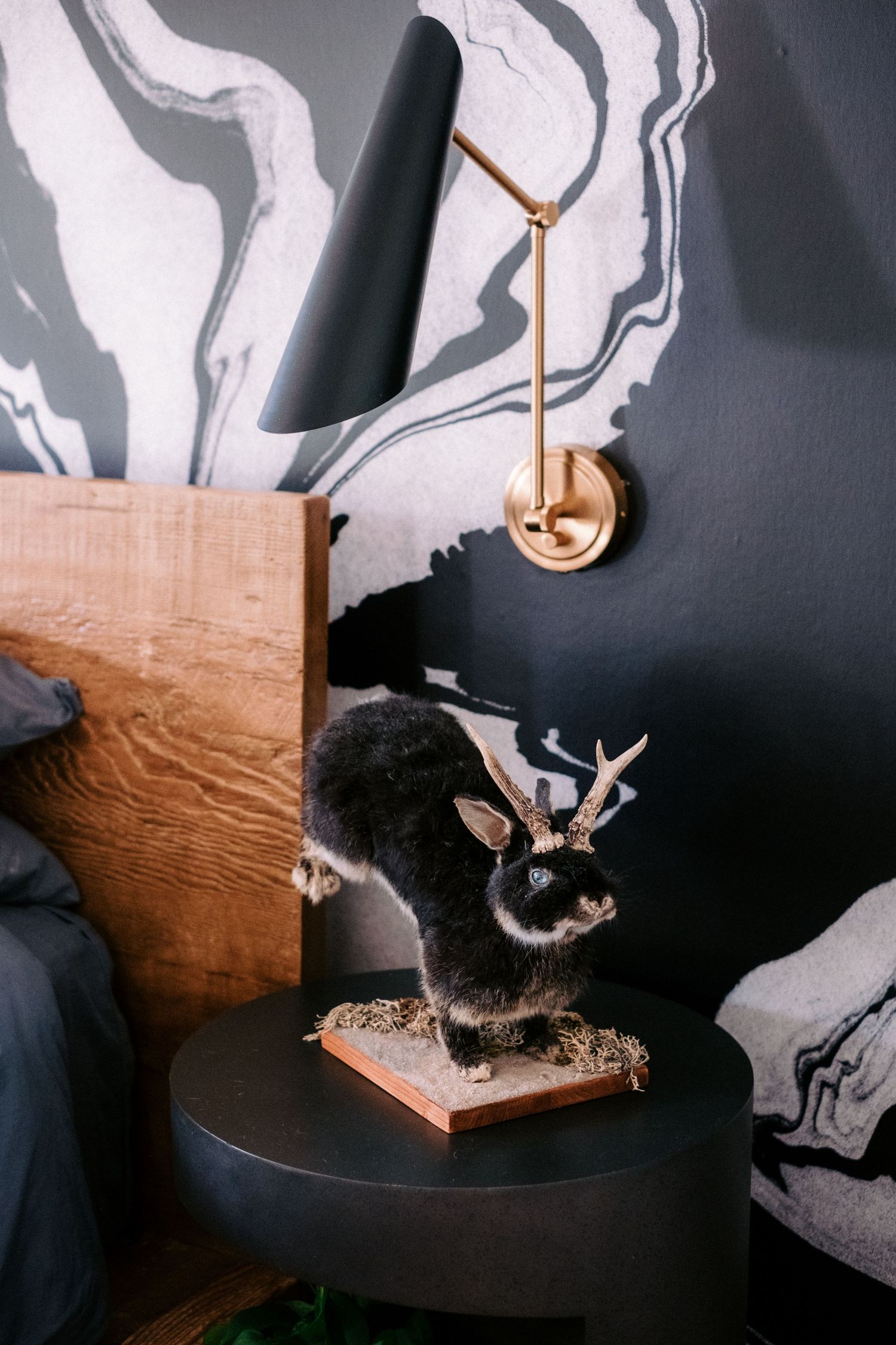Black cat playing with wooden wall-mounted cat toy against marbled wallpaper.