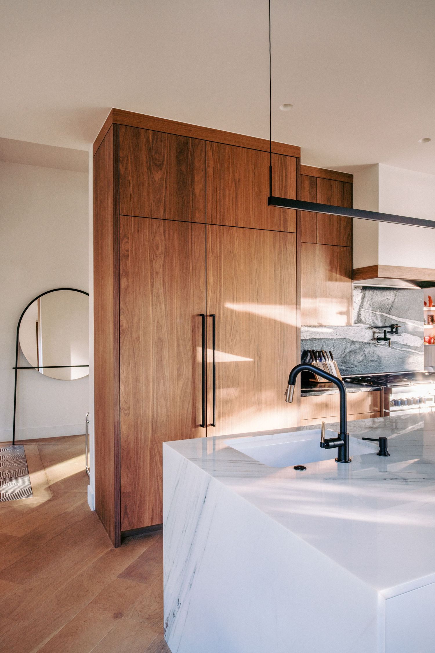 Contemporary kitchen with walnut cabinetry and white marble waterfall countertop.