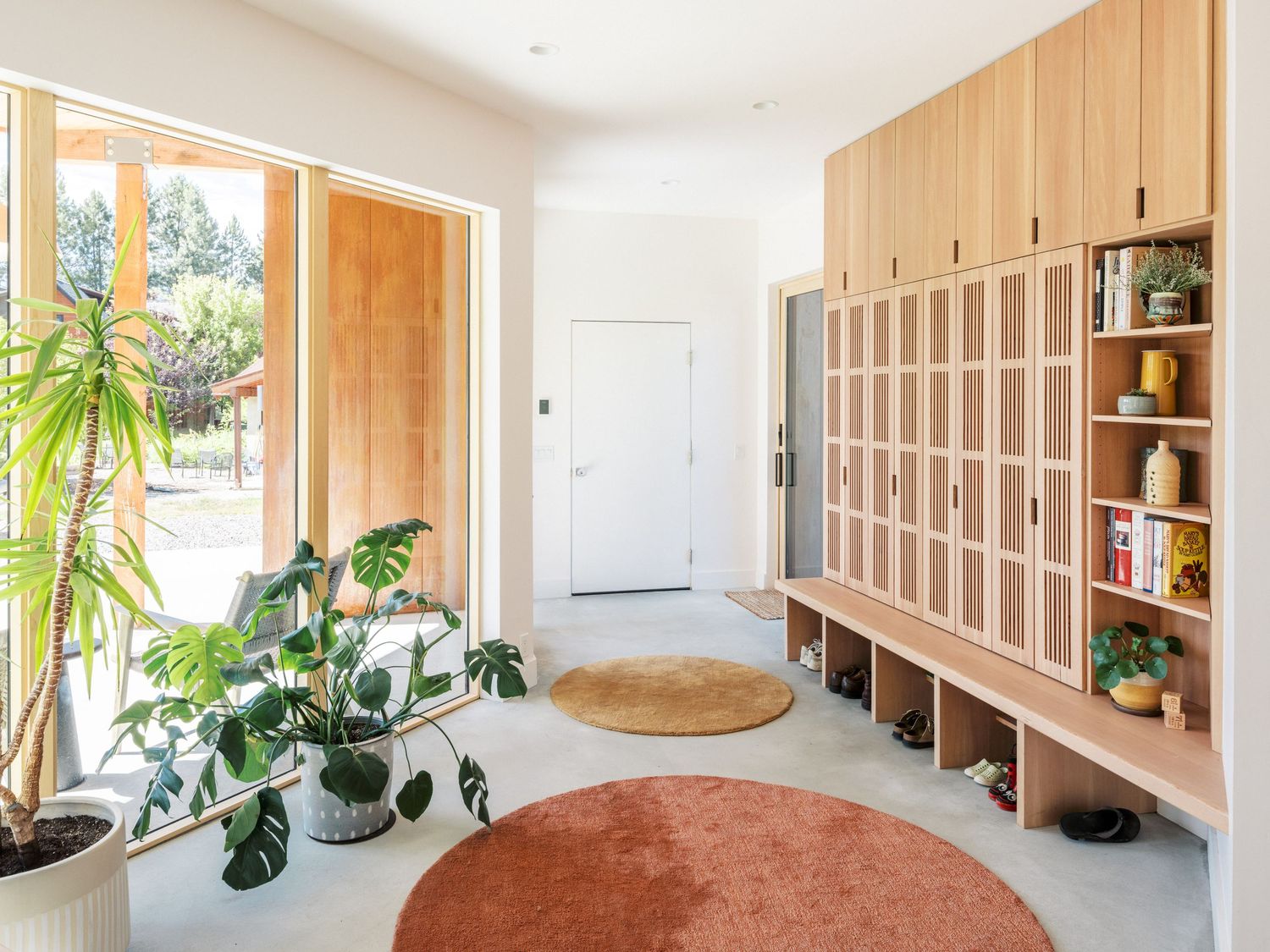 Bright interior hallway with wooden built-ins, indoor plants and natural light from large windows.