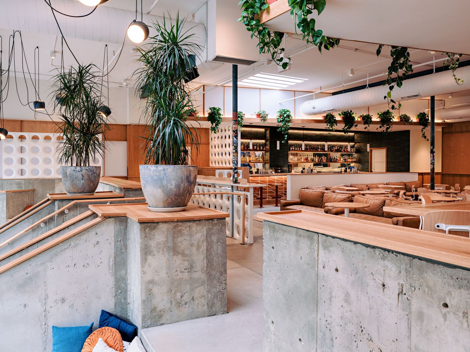 Industrial-style dining space with exposed concrete pillars, hanging plants, and modern furnishings.