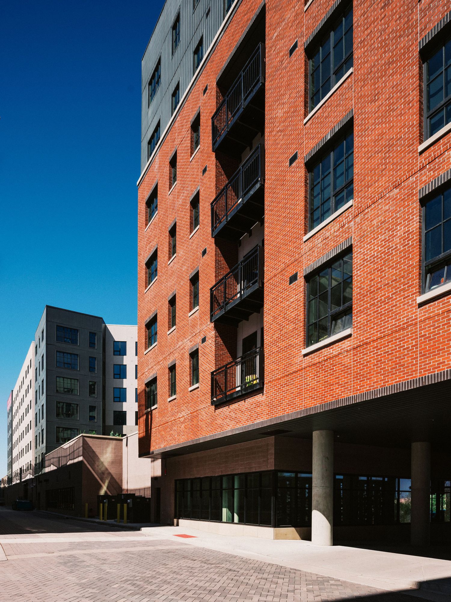 Modern red brick apartment building with angular architecture and concrete walkway.