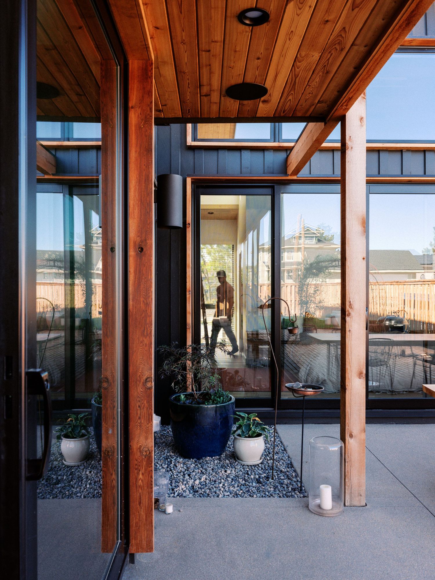 Modern patio space with wooden beam architecture and floor-to-ceiling glass windows overlooking urban setting.