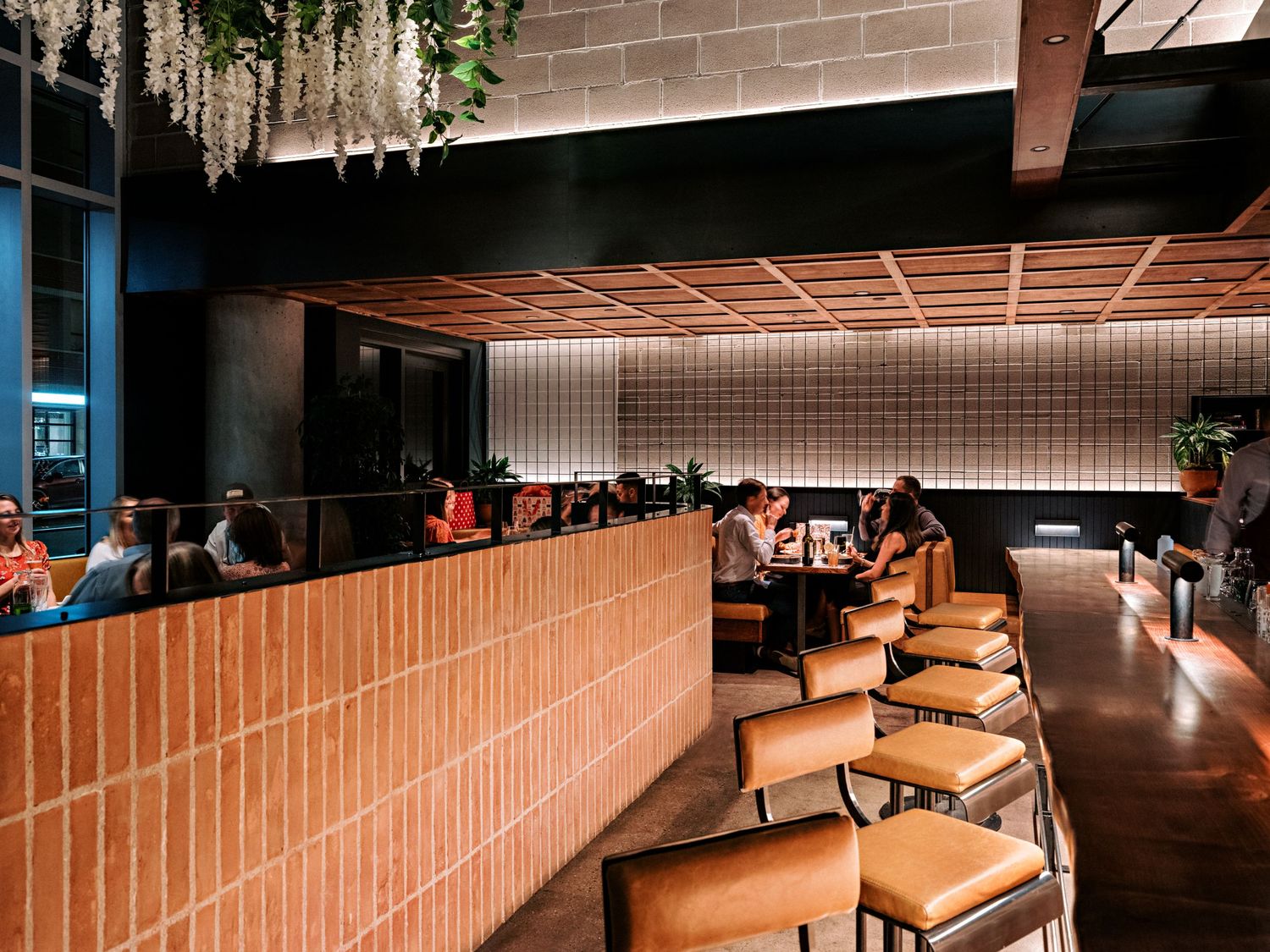 Upscale restaurant interior featuring tan leather seating and hanging botanical decor.