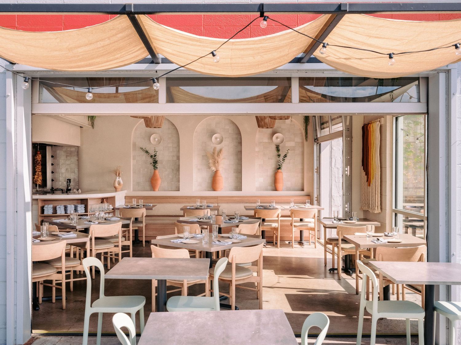 Contemporary dining space with white tables and chairs under hanging fabric canopies.
