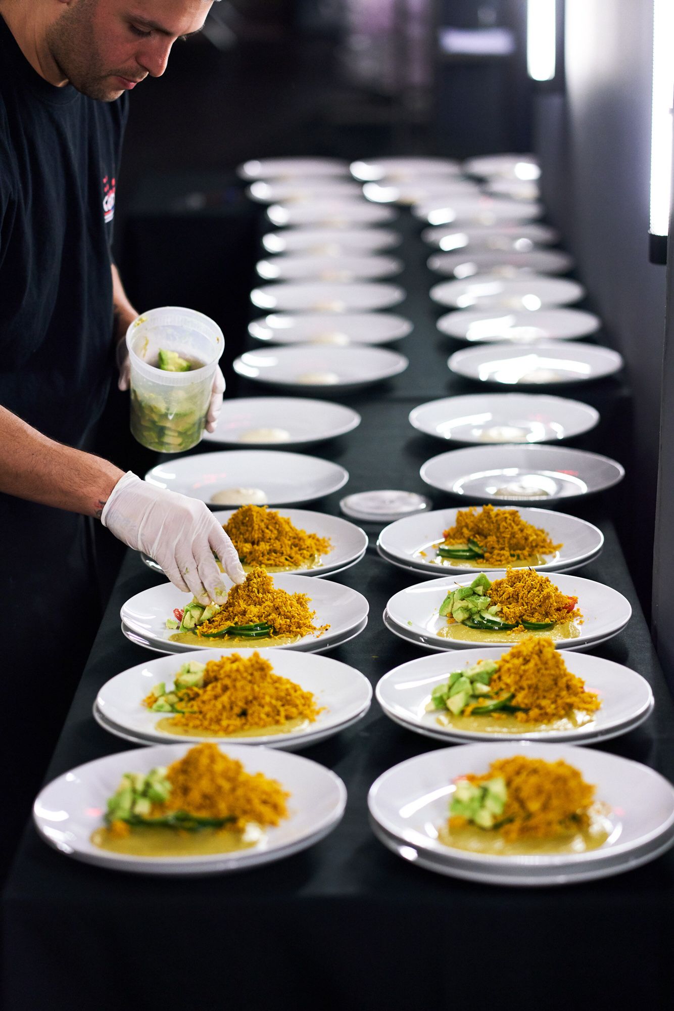 Chef plating gourmet dishes with yellow rice and greens on white plates at a catering event.