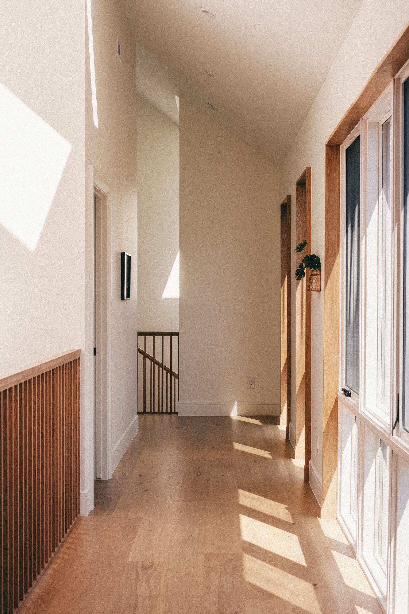 Bright modern hallway with hardwood floors, white walls, wooden accents, and natural light streaming through windows.