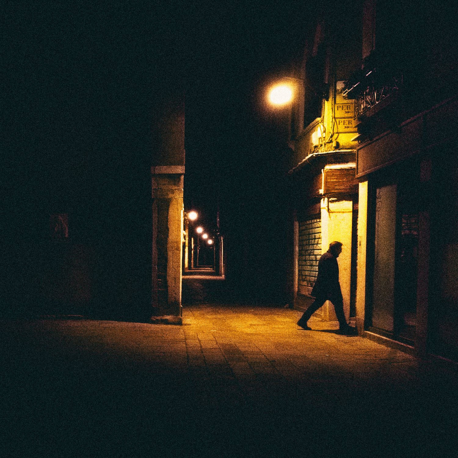 Dark urban alleyway at night with scattered street lights casting dramatic shadows and silhouettes.