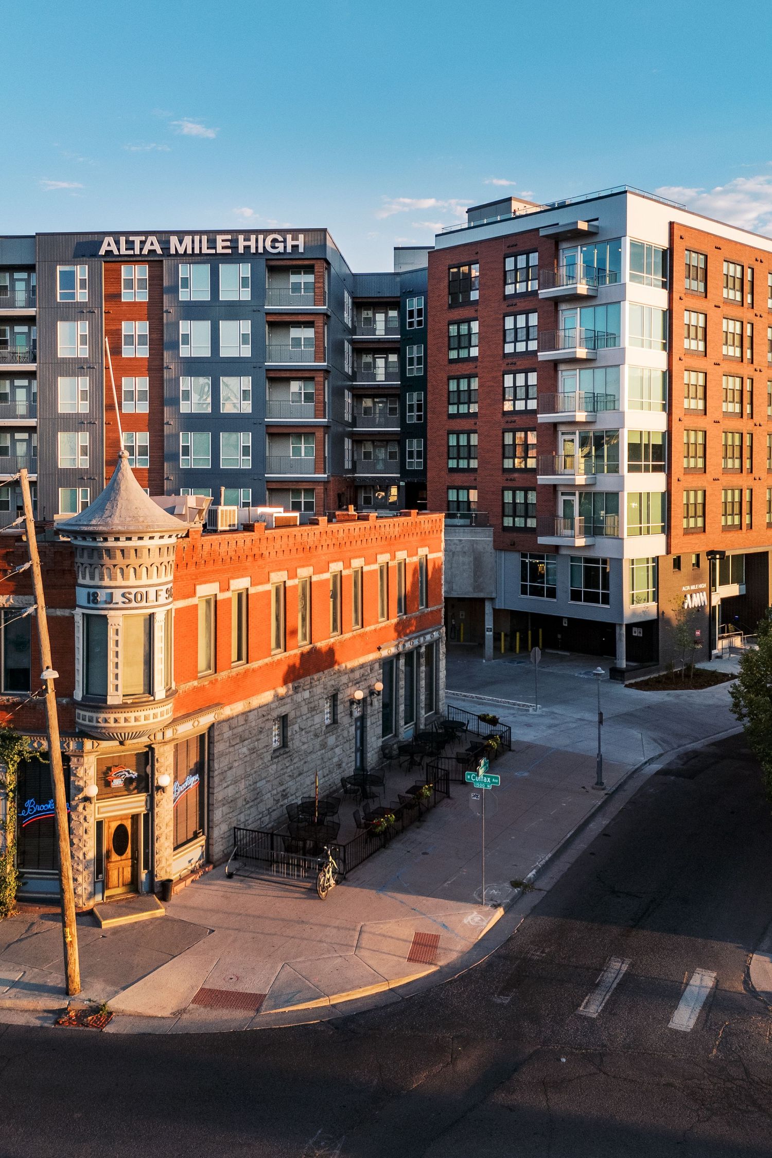 Historic brick building with turret alongside modern apartment complex in urban setting.
