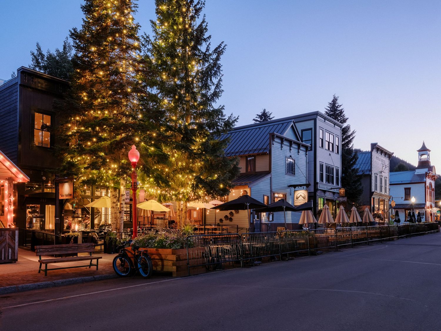 Panoramic view of small town street with illuminated storefronts at dusk.