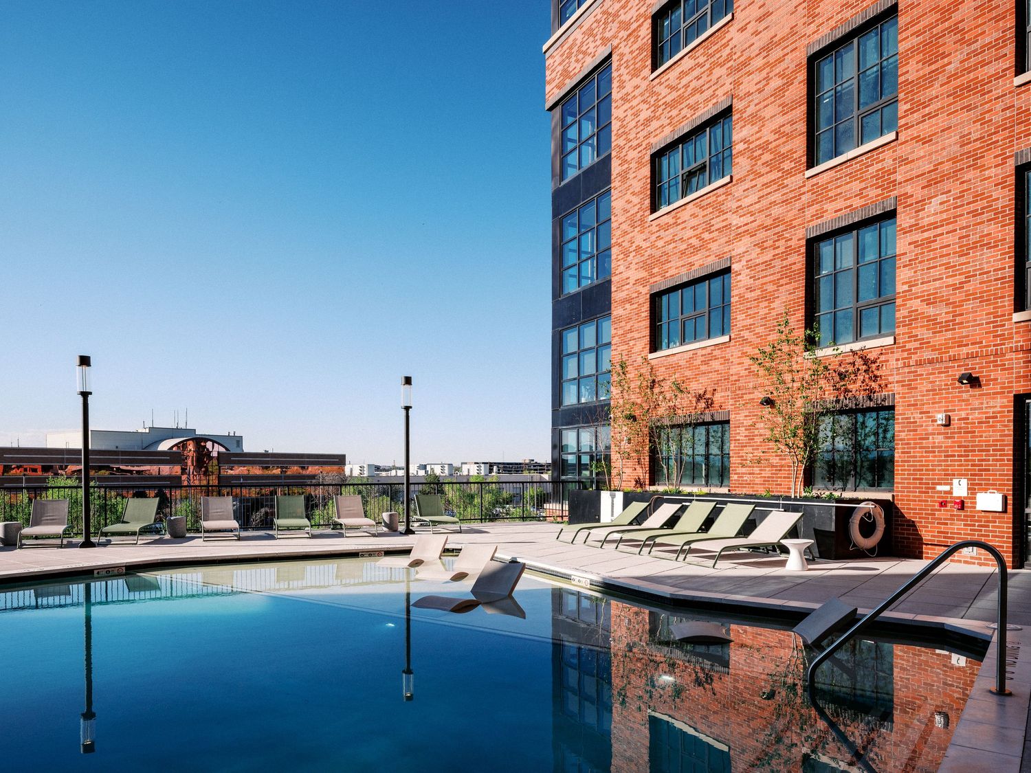 Rooftop swimming pool with lounge chairs against red brick apartment building.