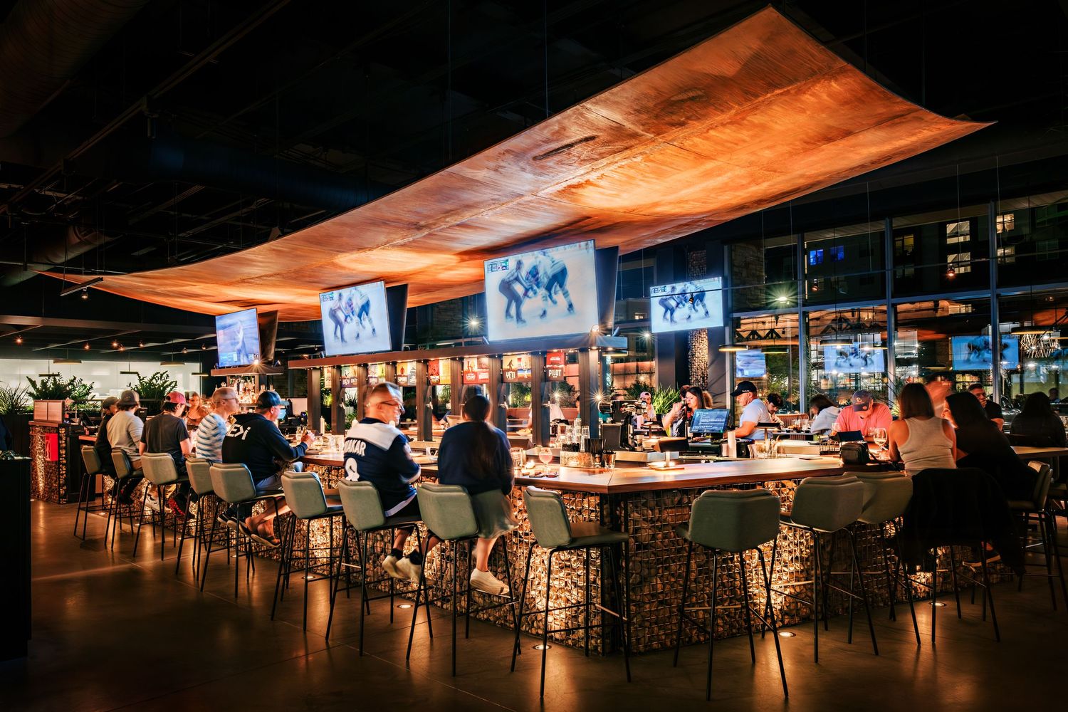 Bustling sports bar with curved ceiling and multiple TV screens showing games.