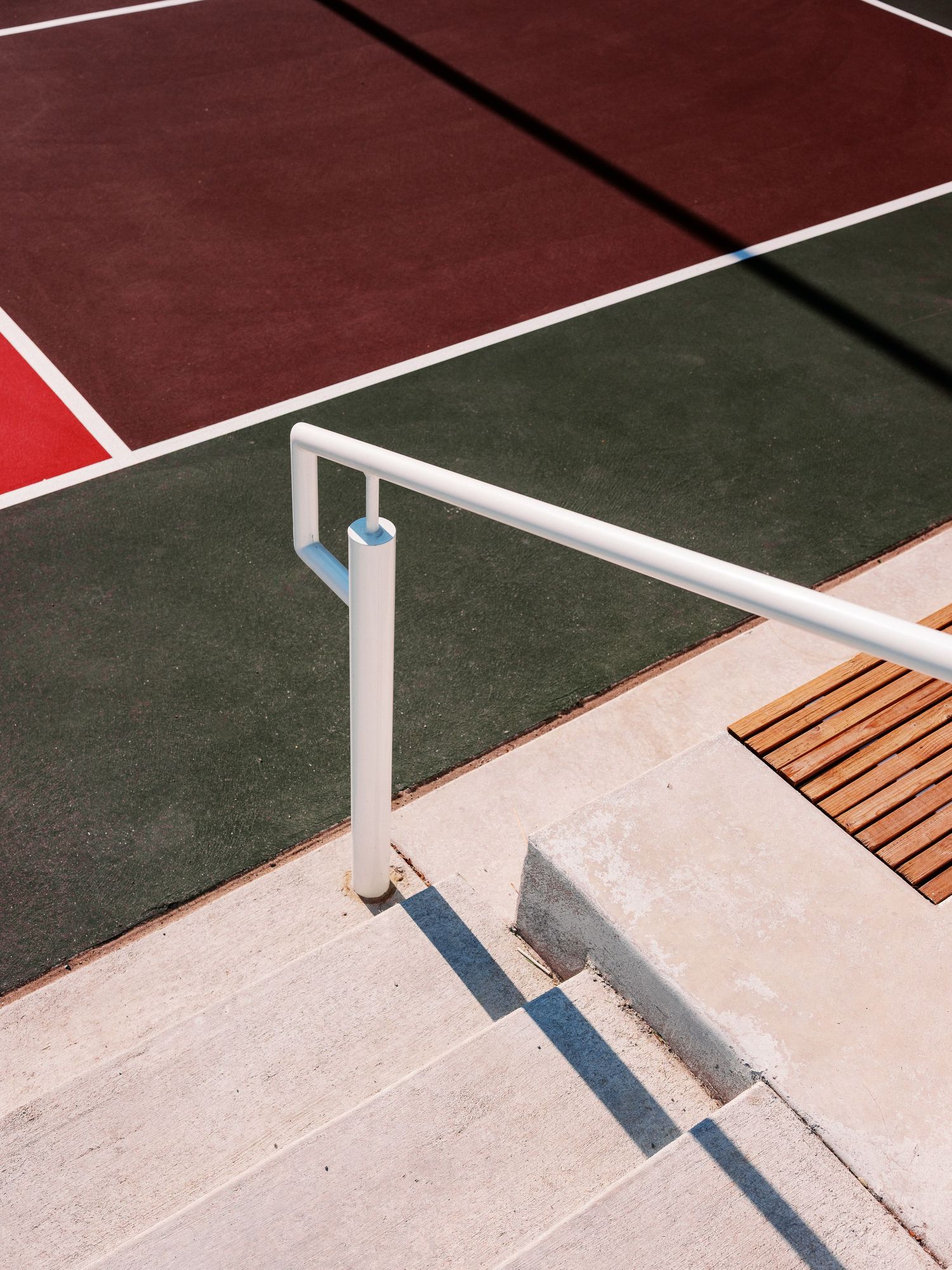 Tennis court boundary lines with white posts casting shadows on concrete and artificial turf.