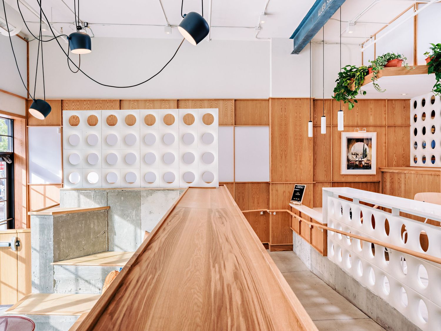 Modern restaurant interior with wood paneling, white geometric wall details, and hanging plants creating a warm atmosphere.