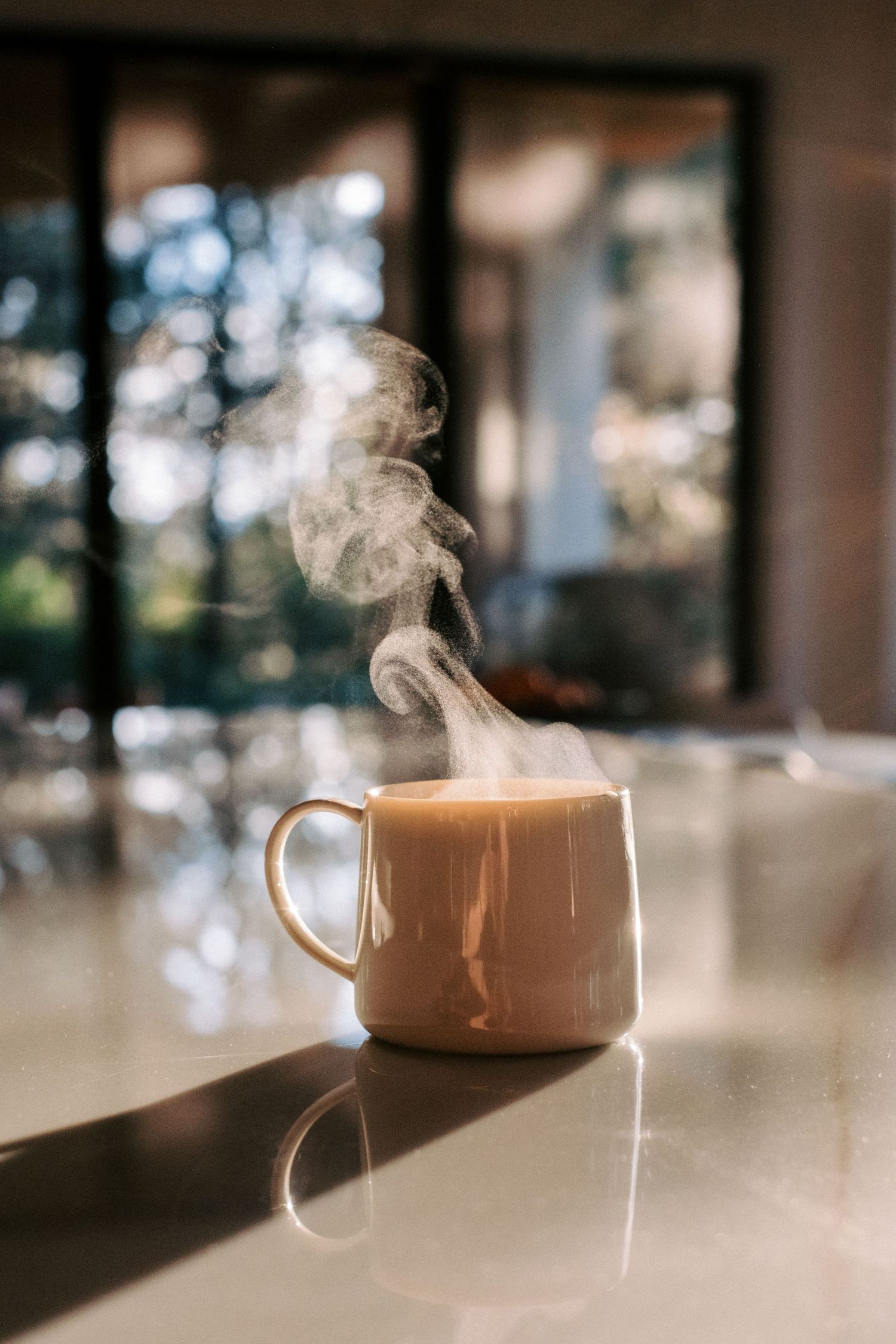 Steaming hot coffee cup on a wooden table with soft natural lighting and rising vapor.