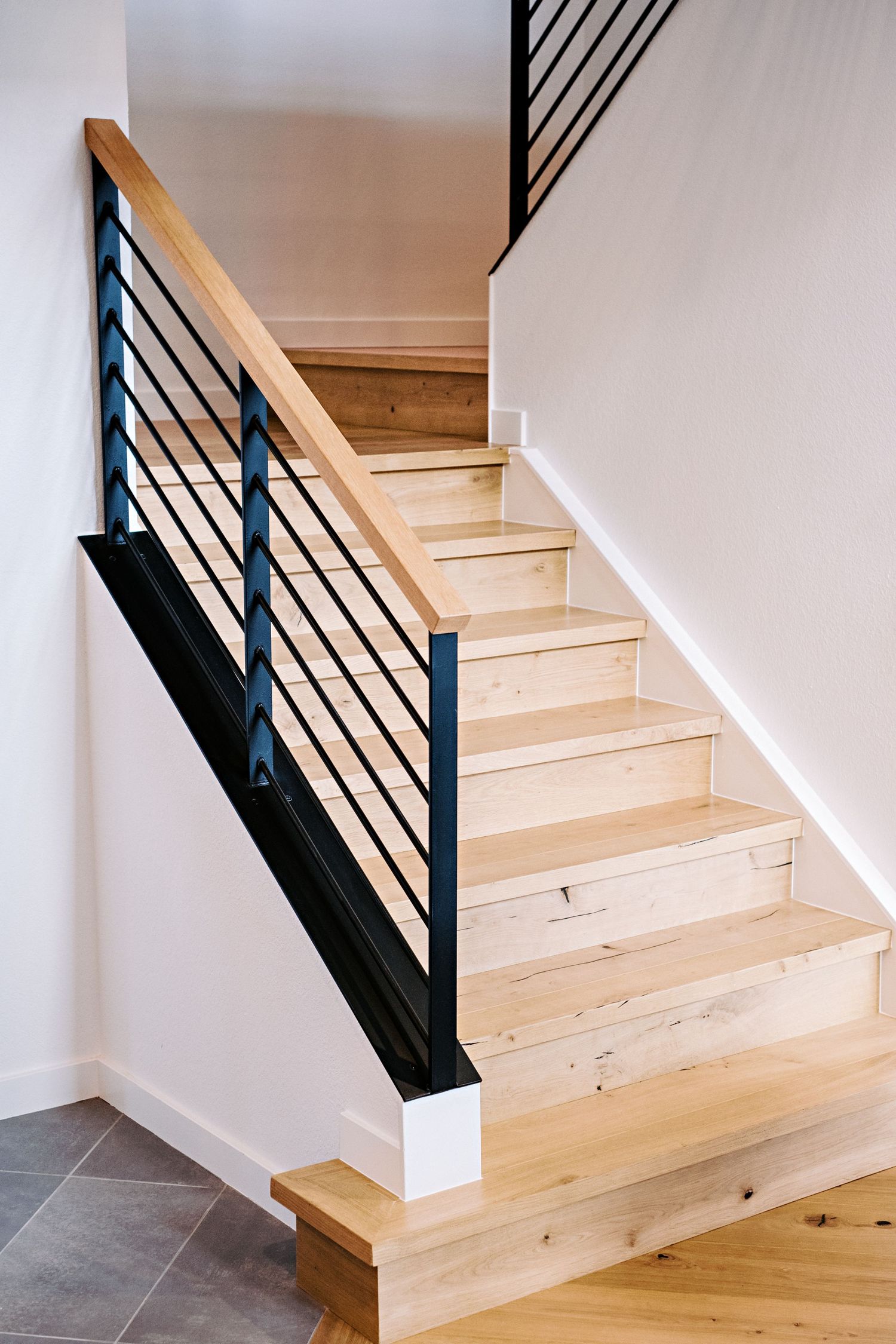 Modern wooden staircase with black metal railings and light natural wood treads in a minimalist interior design.