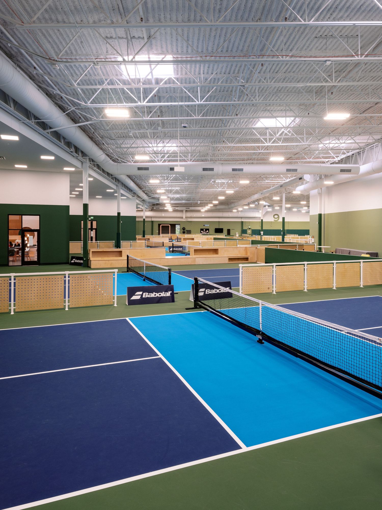 Indoor tennis facility with multiple courts featuring blue and green playing surfaces.