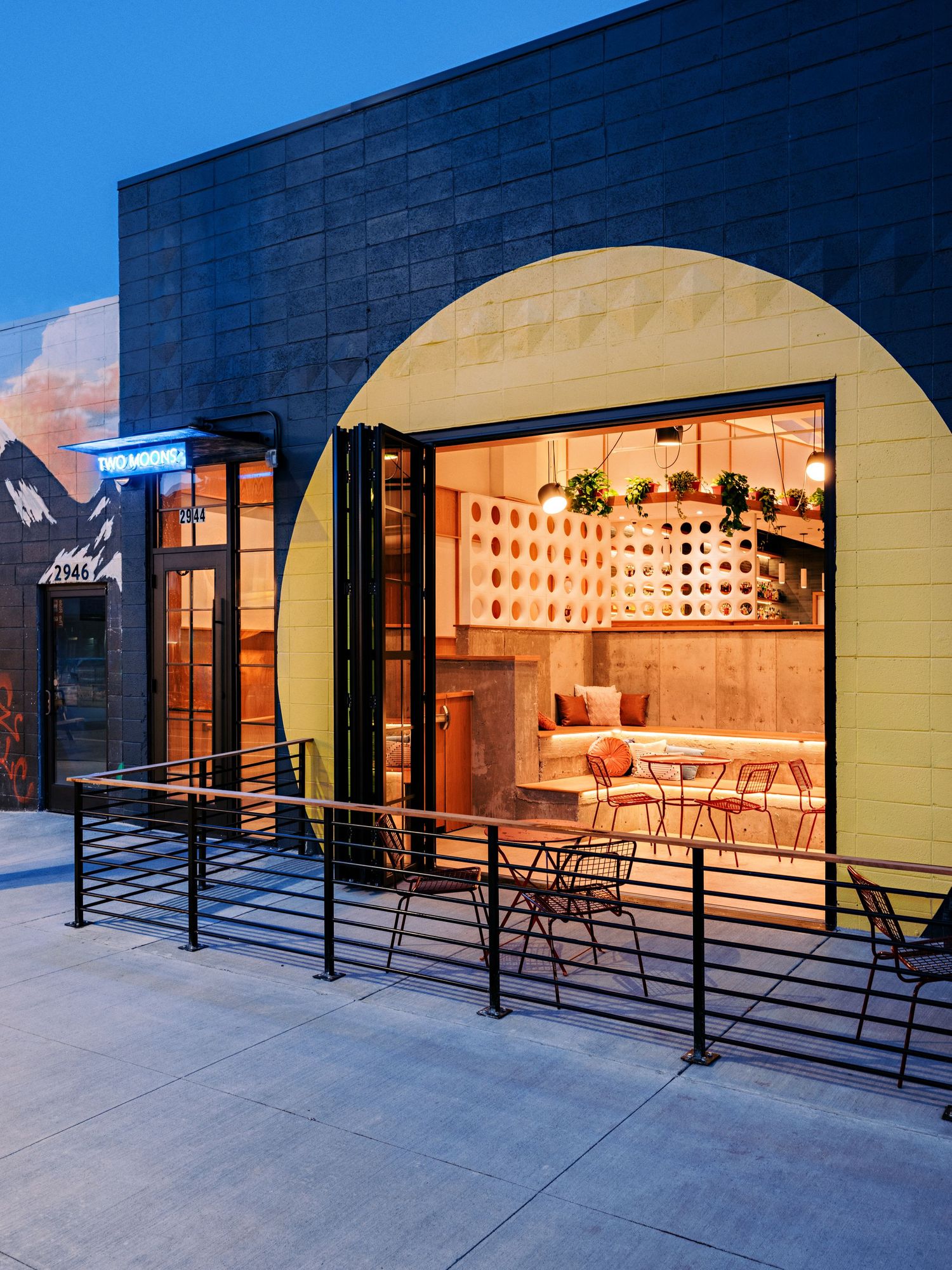 Illuminated storefront with curved archways and outdoor seating area along a modern building facade.
