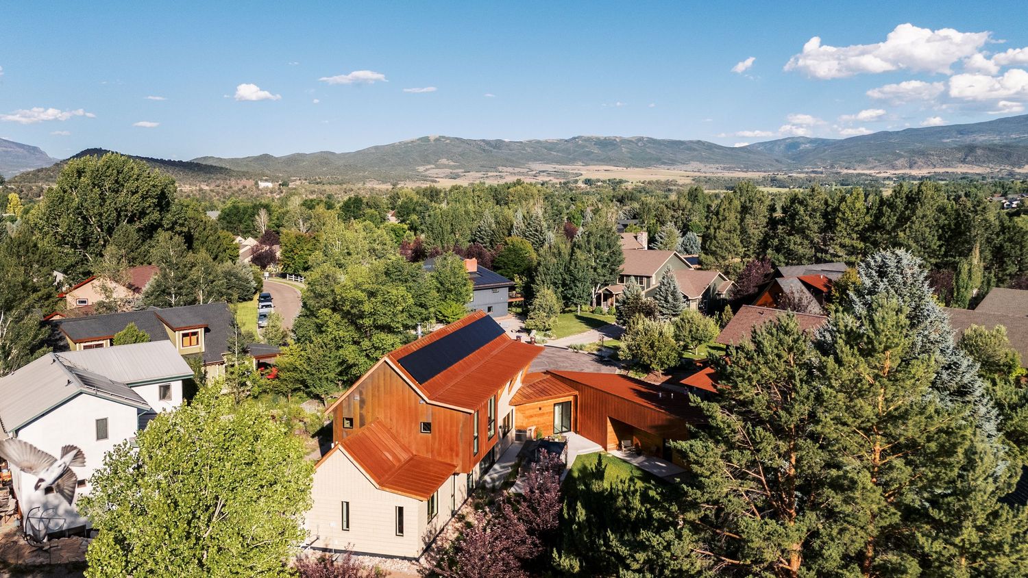 Panoramic mountain landscape view with residential buildings nestled among trees.