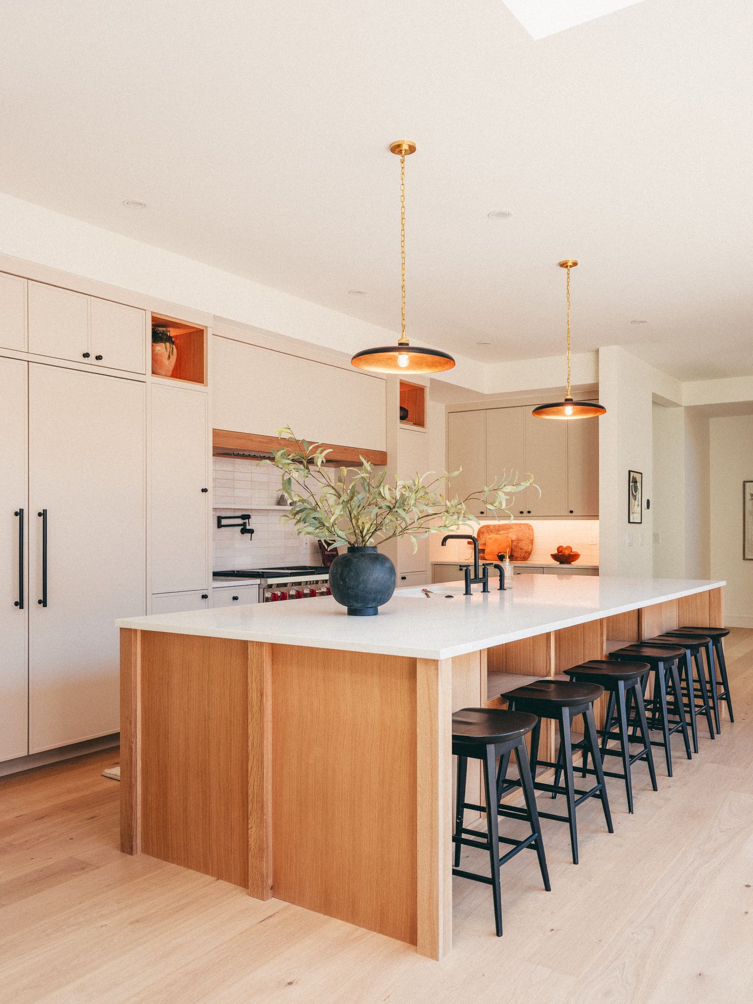 Modern kitchen with large wood island, white countertop, black barstools, pendant lights, and light wood cabinetry.