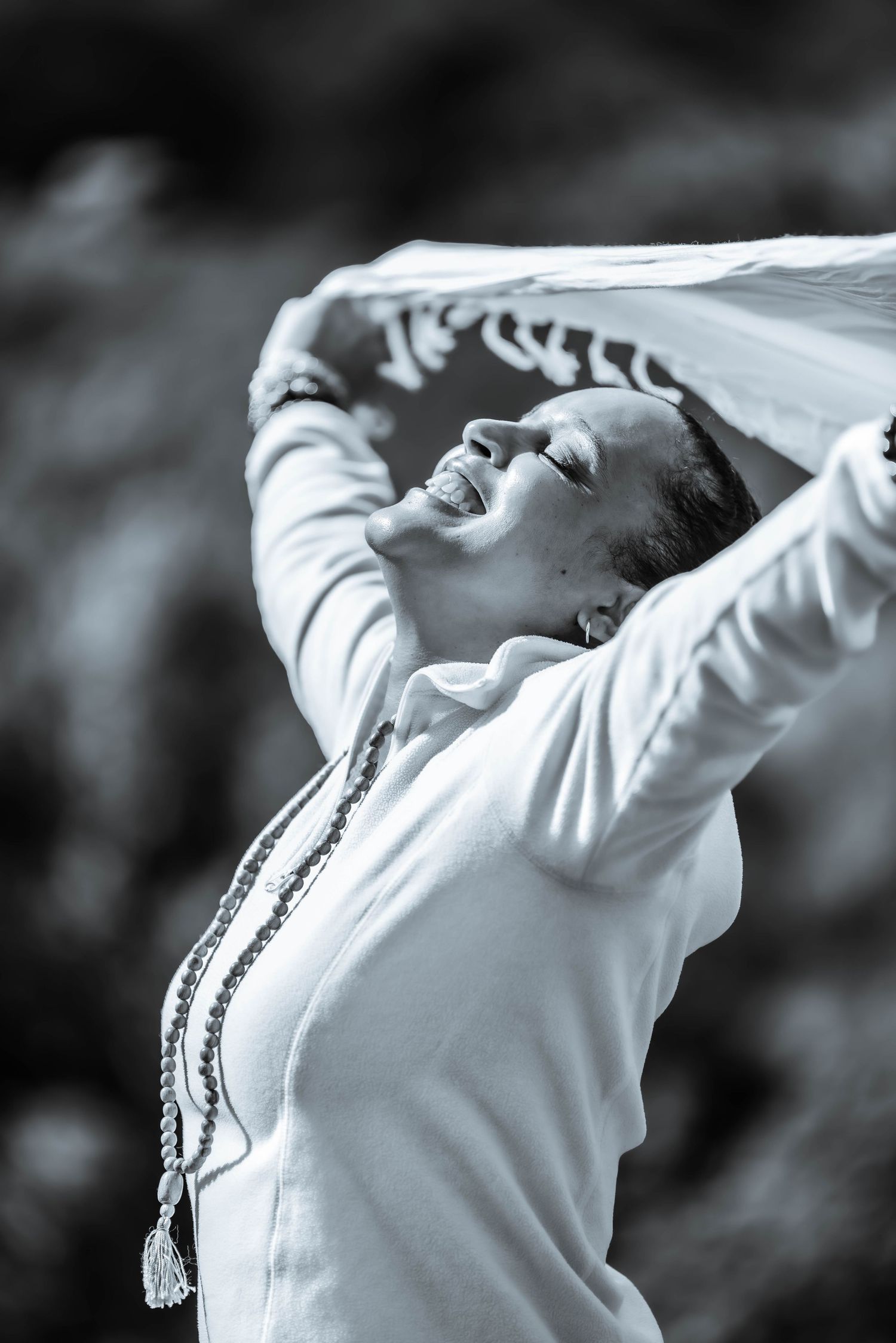 Person in white clothing stretching with arms raised against dark background.