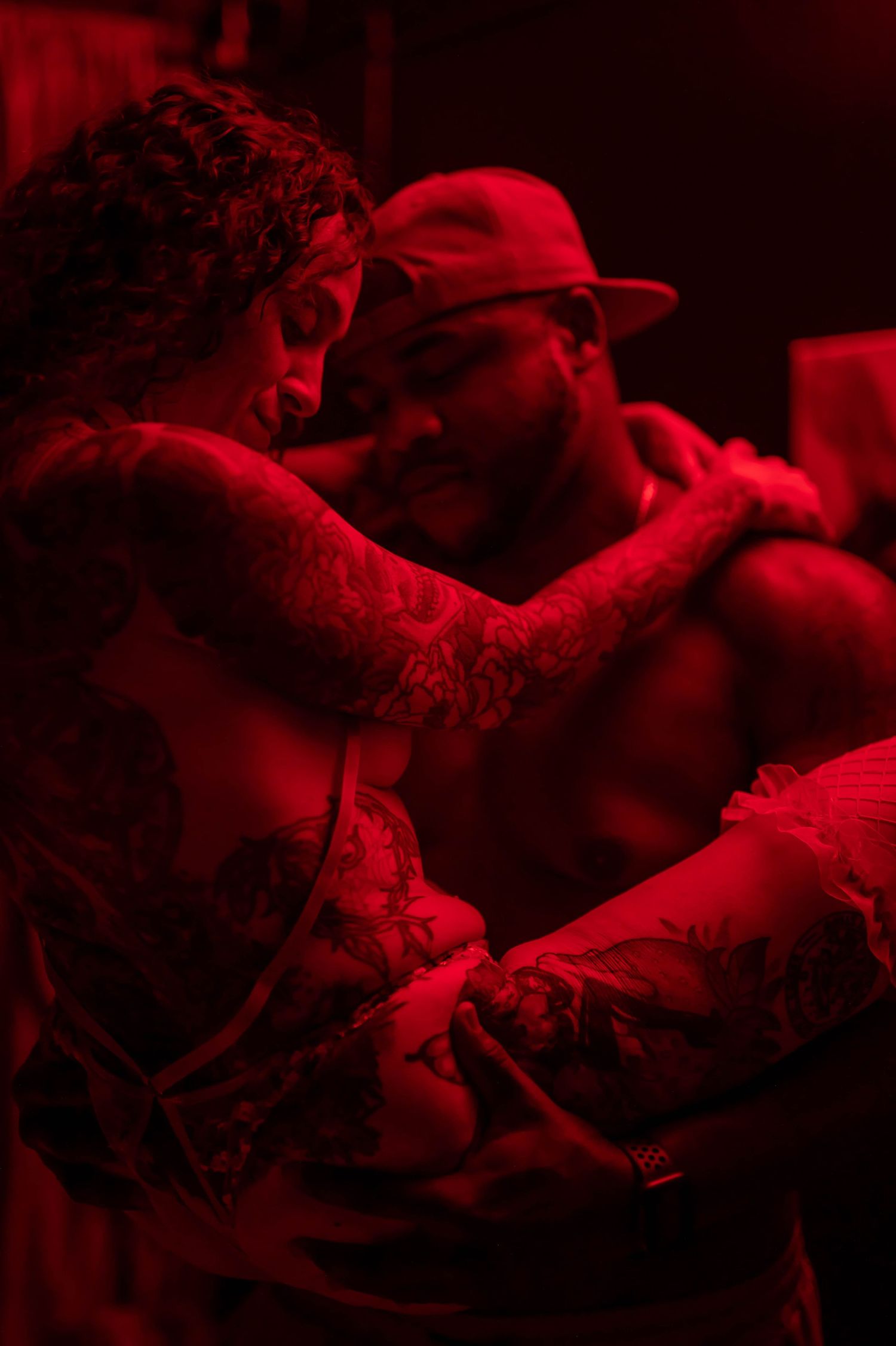 Intimate portrait bathed in deep red lighting with dramatic shadows.