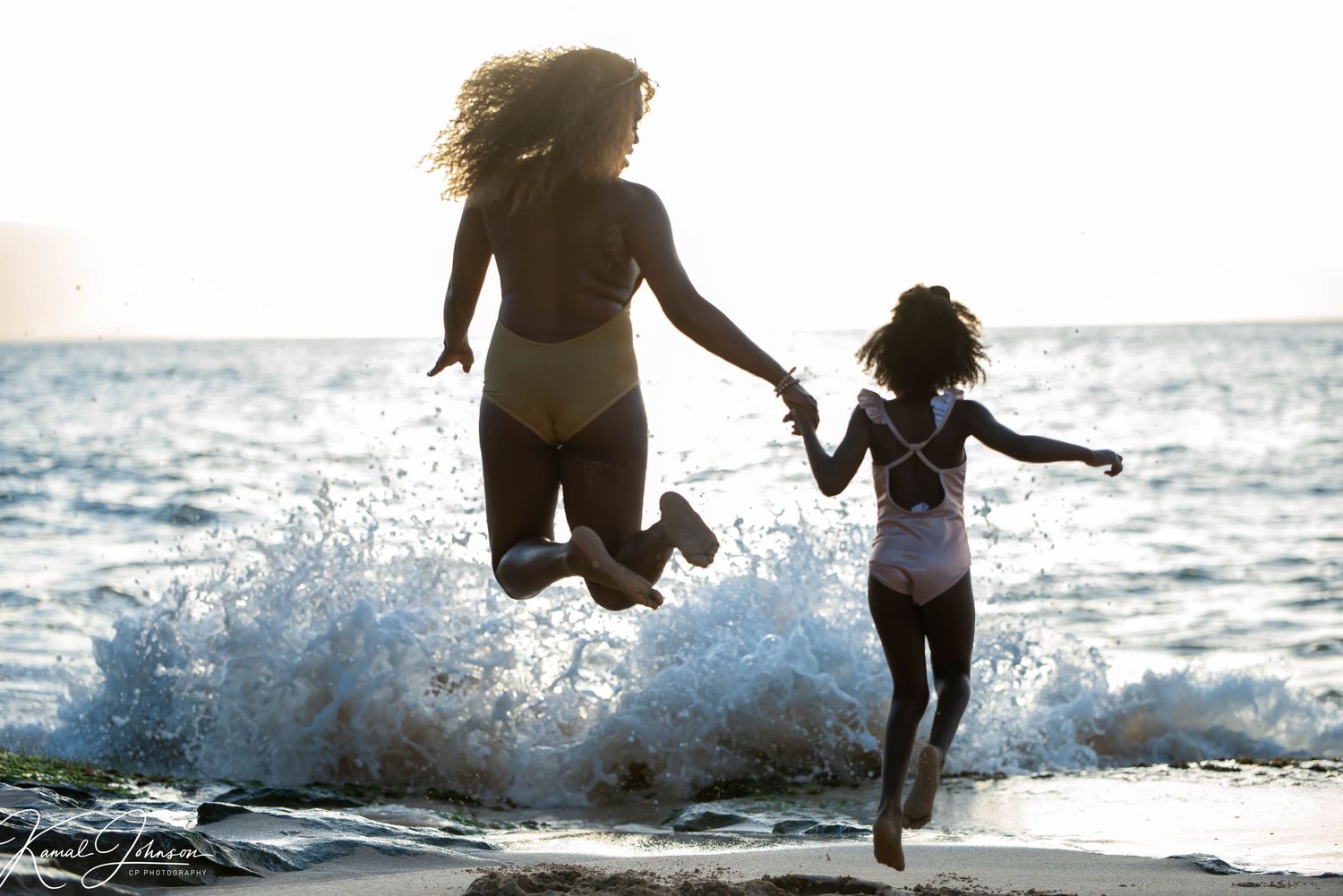 Silhouetted figures joyfully playing and splashing in ocean waves at sunset.