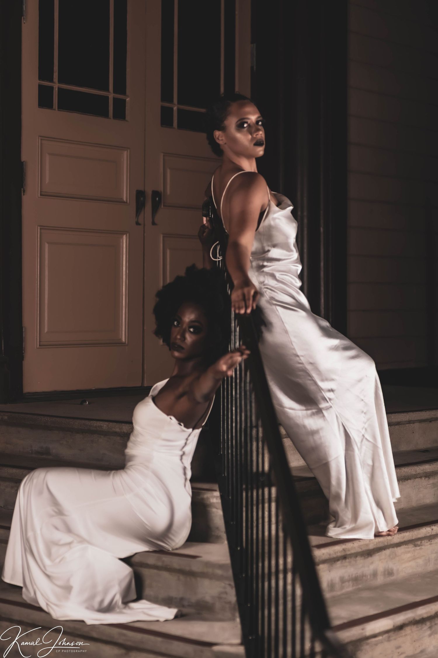 Woman in white dress poses dramatically on vintage building steps in moody lighting.