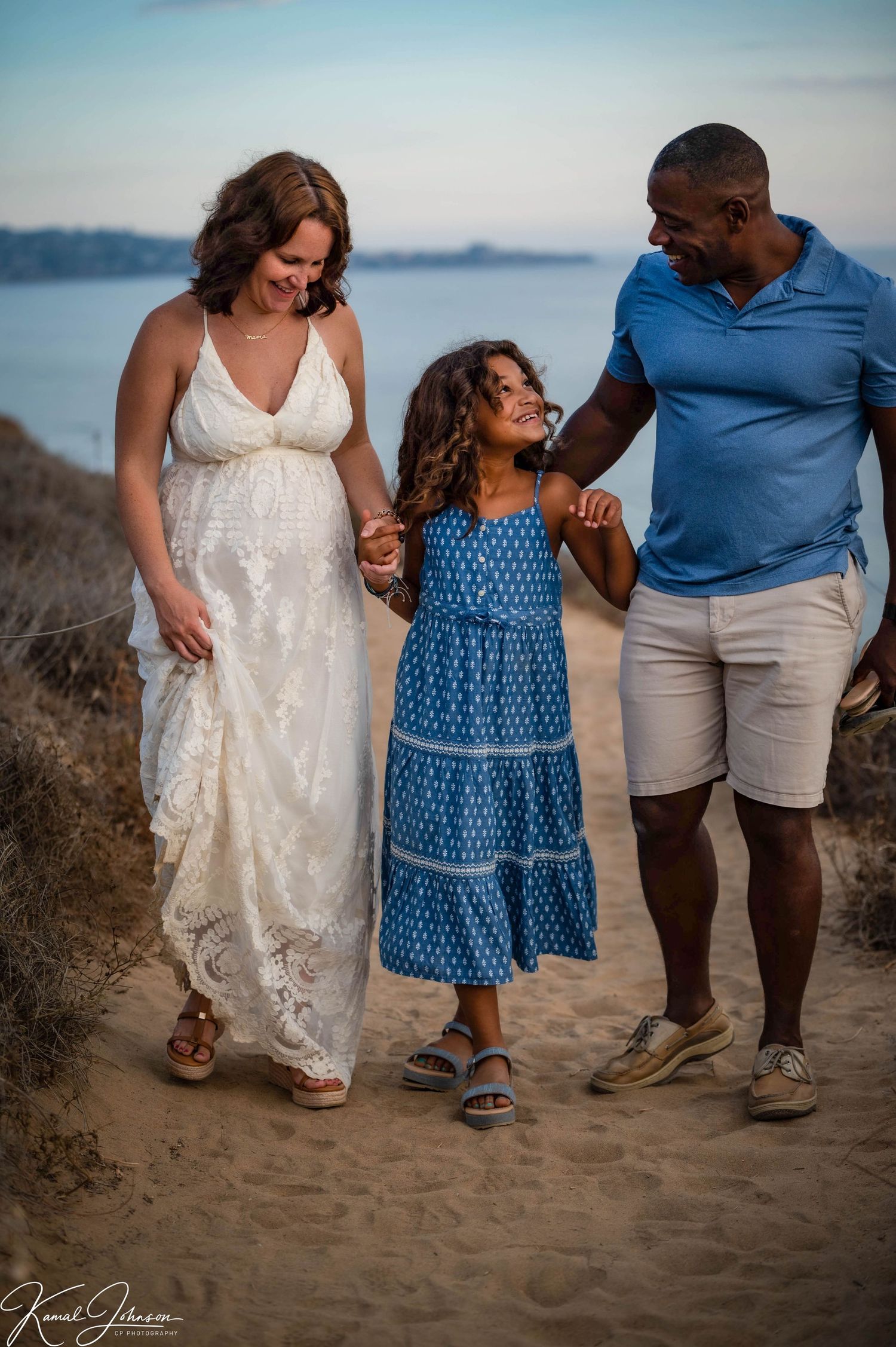Family walking together on coastal trail at sunset wearing casual summer outfits.