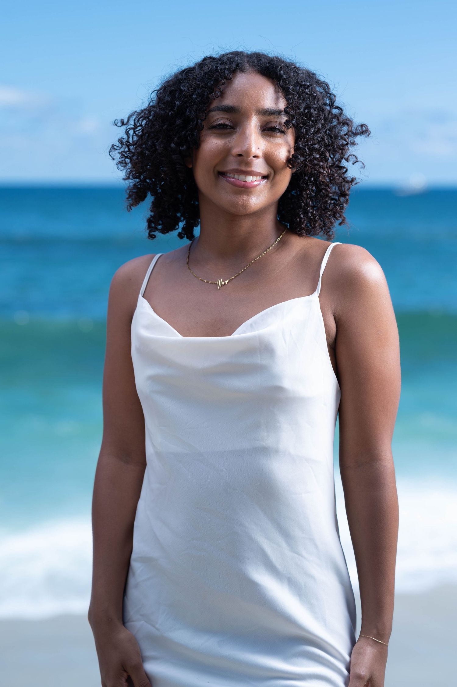Summer beach portrait in white tank top with ocean waves in background.