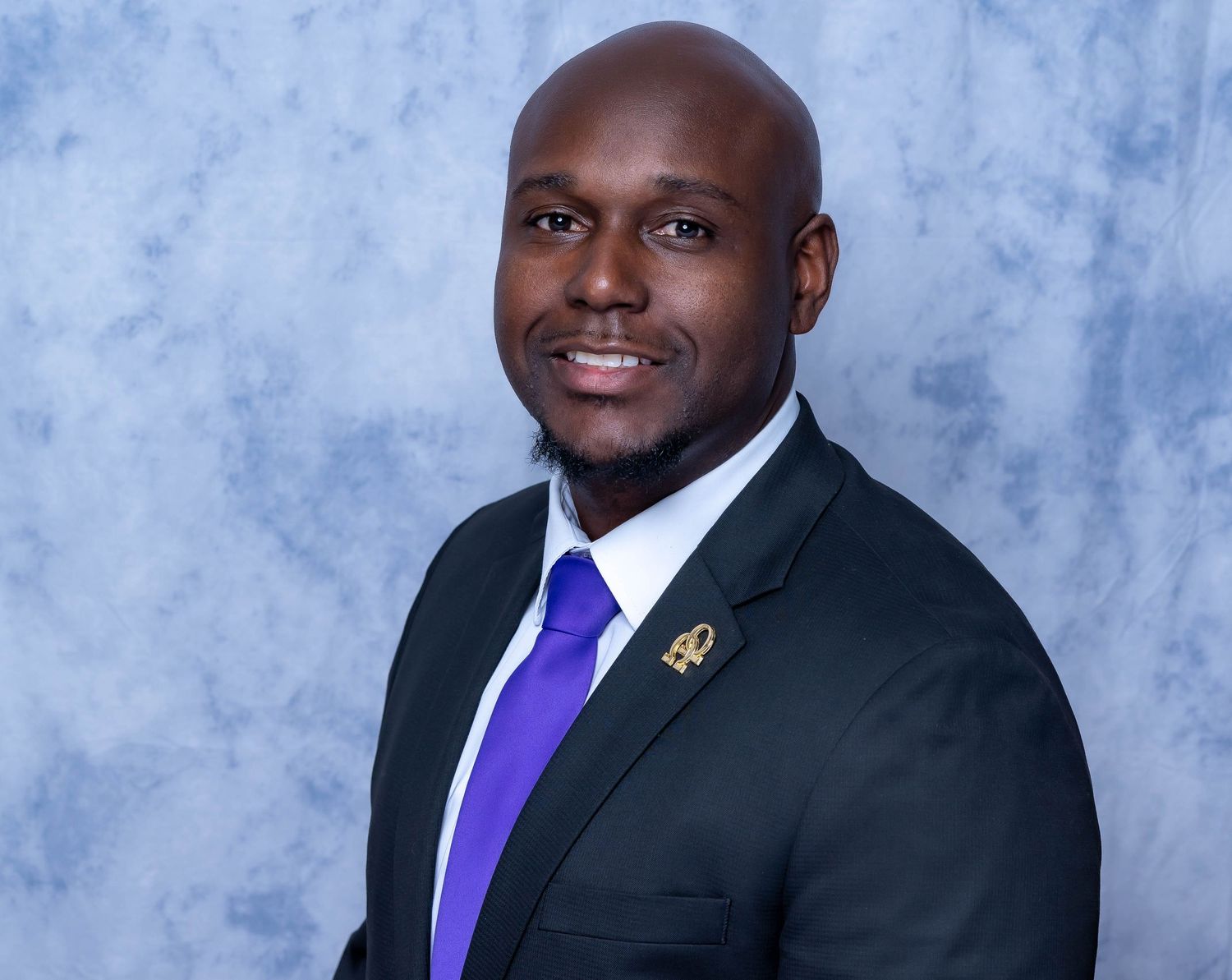 Executive portrait of person wearing black suit with purple tie against studio background.