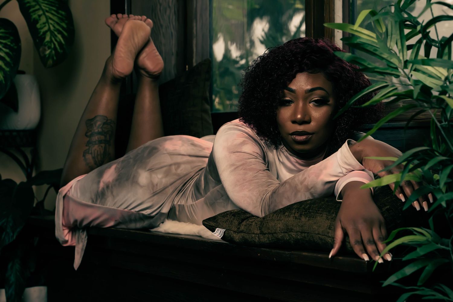 A person in a pink top reclines on a dark bench surrounded by lush tropical greenery and foliage.