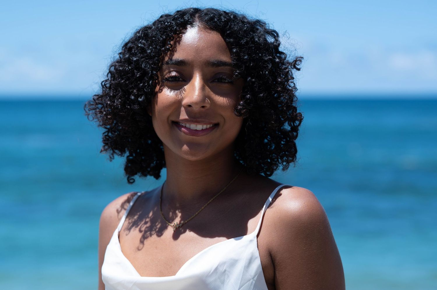 Beachside portrait with natural curly hair against blue ocean background.