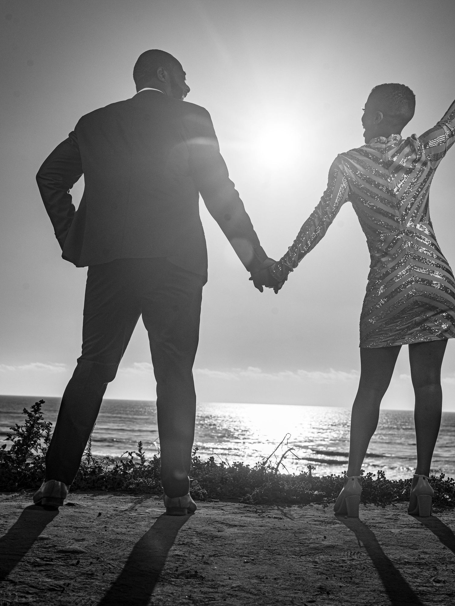 Silhouetted figures holding hands on a beach at sunset with ocean waves in the background.