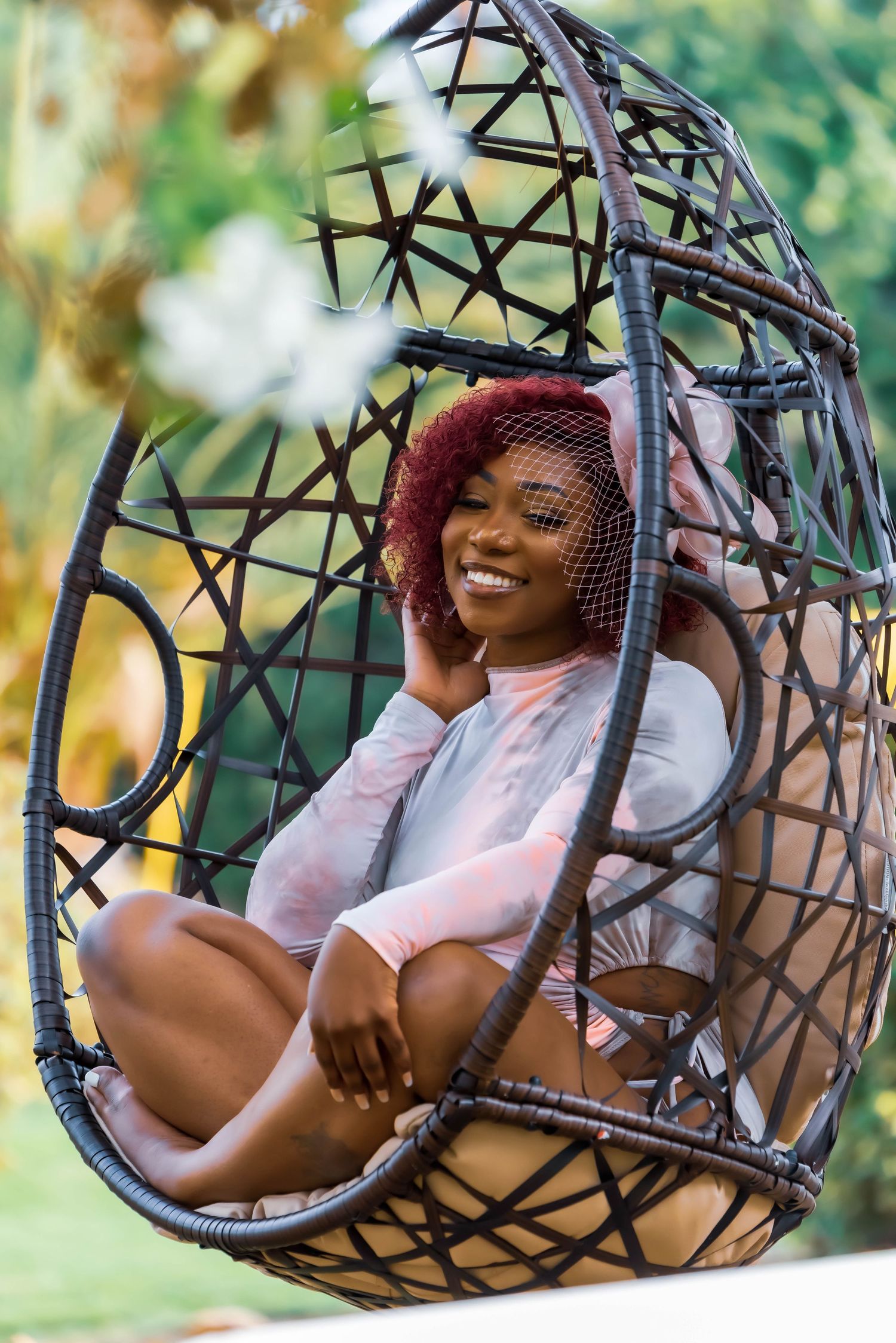 Person relaxing in outdoor hanging egg chair with lush greenery in background.