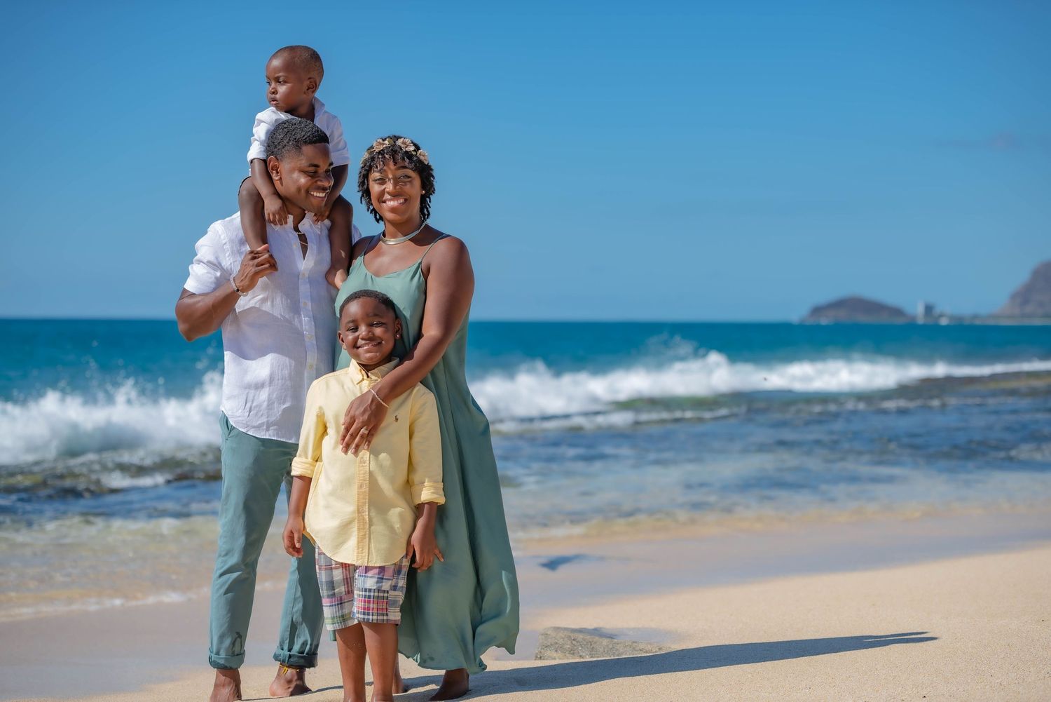 Family walking along scenic beach with waves and blue sky.