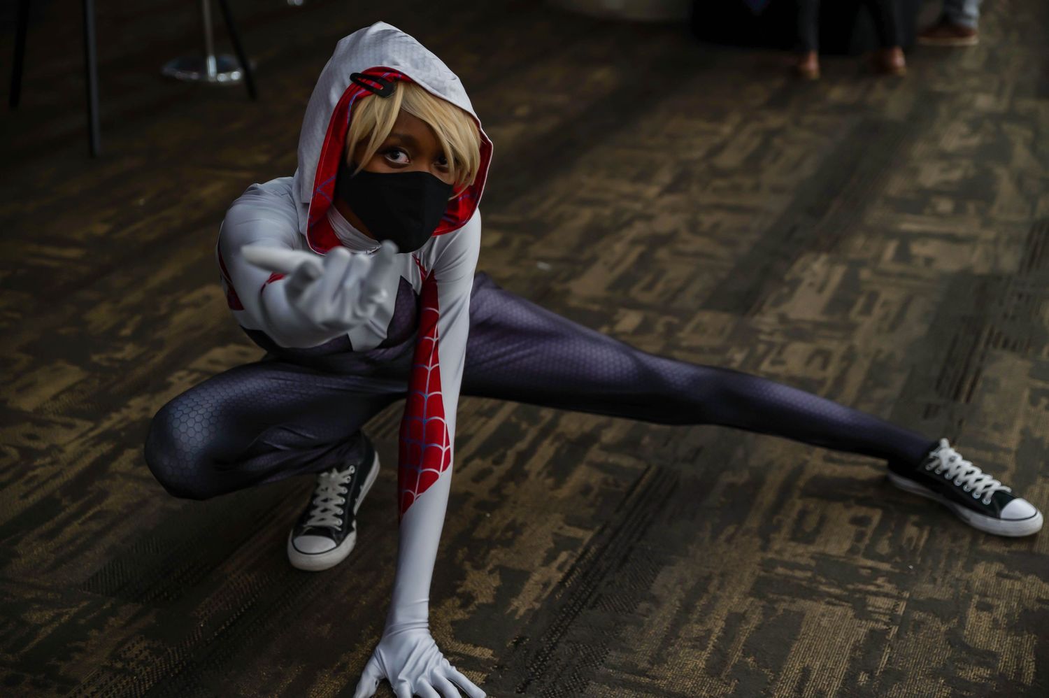 A person in athletic wear and sneakers stretches on a wooden floor.