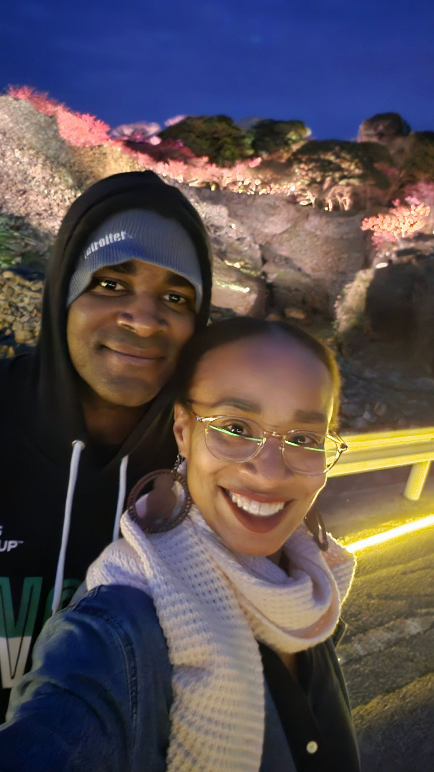 Couple taking a nighttime selfie with illuminated rock formations in the background.